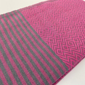 Puede incluir: Una manta de tiro de rayas rosa y gris con un patr&oacute;n geom&eacute;trico. La manta est&aacute; doblada por la mitad y el patr&oacute;n es visible en ambos lados.