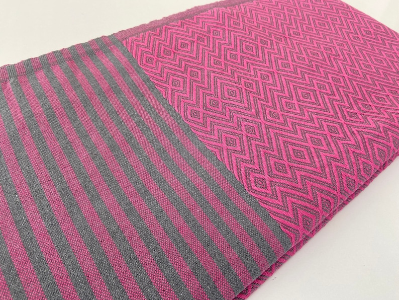 Puede incluir: Una manta de tiro de rayas rosa y gris con un patr&oacute;n geom&eacute;trico. La manta est&aacute; doblada por la mitad y el patr&oacute;n es visible en ambos lados.