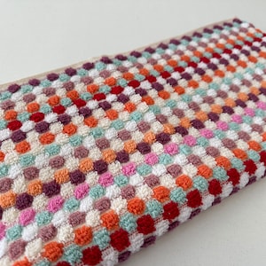 May include: A colorful kitchen towel with a checkered pattern of red, orange, green, white, and purple. The towel is made of a soft, absorbent material.