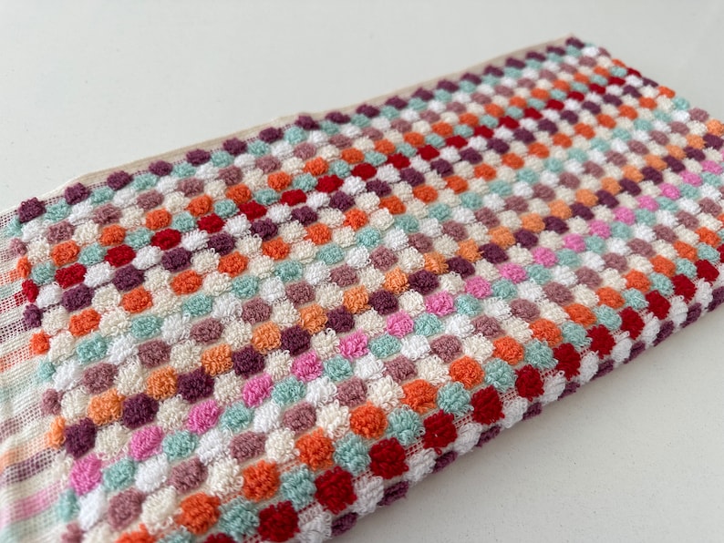 May include: A colorful kitchen towel with a checkered pattern of red, orange, green, white, and purple. The towel is made of a soft, absorbent material.