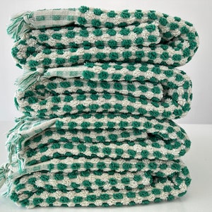 May include: A stack of four green and white checkered towels with a textured surface. The towels are folded and stacked on top of each other.