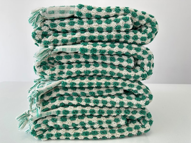 May include: A stack of four green and white checkered towels with a textured surface. The towels are folded and stacked on top of each other.