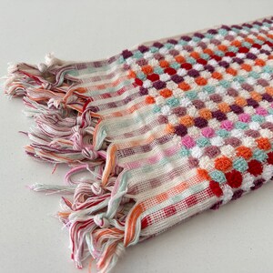 May include: A colorful striped and patterned bath towel with a fringe border. The towel is made of a soft, absorbent material and features a variety of colors, including red, orange, pink, green, and white.