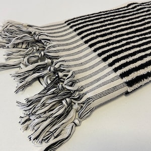 May include: Black and white striped towel with a fringe border. The towel is made of a soft, absorbent material.