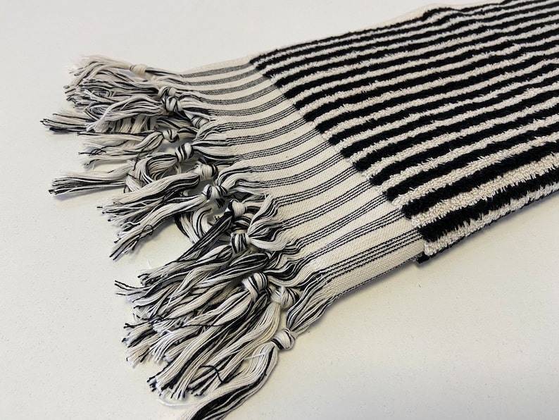 May include: Black and white striped towel with a fringe border. The towel is made of a soft, absorbent material.