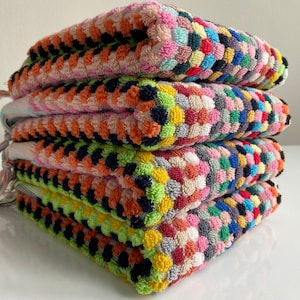 May include: A stack of four colorful, textured square towels. Each towel features a pattern of small, raised circles in various colors, including pink, orange, green, blue, and yellow. The towels have fringe on one side.