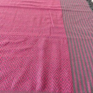 Puede incluir: Una manta de tiro rosa y gris con un patr&oacute;n de diamantes en un lado y rayas grises en el otro.