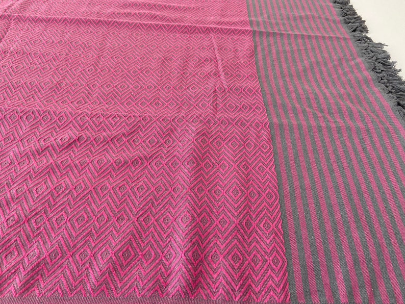 Puede incluir: Una manta de tiro rosa y gris con un patr&oacute;n de diamantes en un lado y rayas grises en el otro.