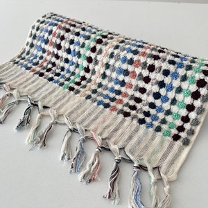 K&ouml;nnte beinhalten: Ein wei&szlig;es Badetuch mit einem bunten geometrischen Muster aus blauen, gr&uuml;nen, rosa und schwarzen Kreisen. Das Handtuch hat einen Fransenrand.