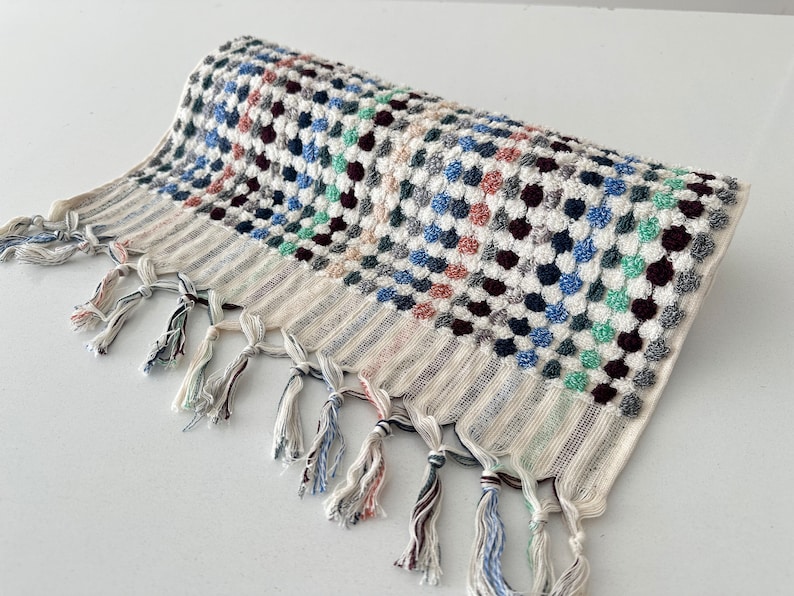 K&ouml;nnte beinhalten: Ein wei&szlig;es Badetuch mit einem bunten geometrischen Muster aus blauen, gr&uuml;nen, rosa und schwarzen Kreisen. Das Handtuch hat einen Fransenrand.