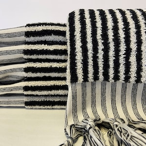 May include: A stack of black and white striped towels with fringe. The towels are made of a soft, absorbent material.