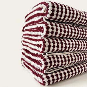May include: A stack of five folded bath towels. The towels have a pattern of alternating burgundy and white stripes and dots. The towels are stacked neatly on top of each other, with the top towel rolled.