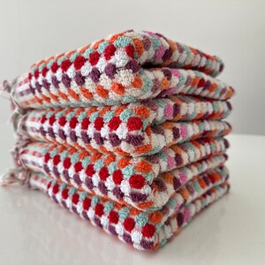 May include: A stack of five colorful kitchen towels with a geometric pattern in shades of red, orange, white, green, and purple.