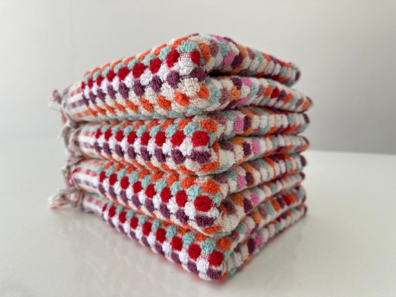 May include: A stack of five colorful kitchen towels with a geometric pattern in shades of red, orange, white, green, and purple.
