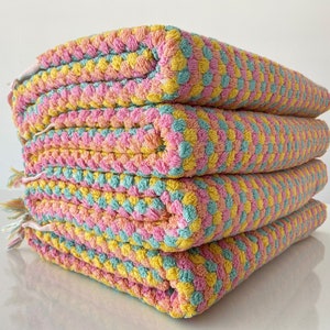May include: A stack of four colorful towels in pink, yellow, and green. The towels are made of a soft, fluffy material and have a waffle-like texture.