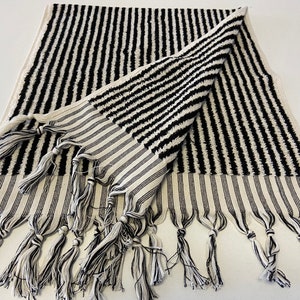 May include: Black and white striped towel with fringe. The towel is folded in half and has a textured surface.