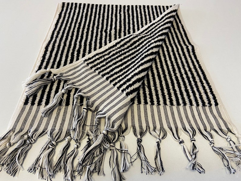 May include: Black and white striped towel with fringe. The towel is folded in half and has a textured surface.
