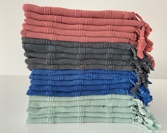 Könnte beinhalten: Ein Stapel aus vier verschiedenen farbigen Handtüchern mit Quasten. Die Handtücher sind rosa, grau, blau und grün.