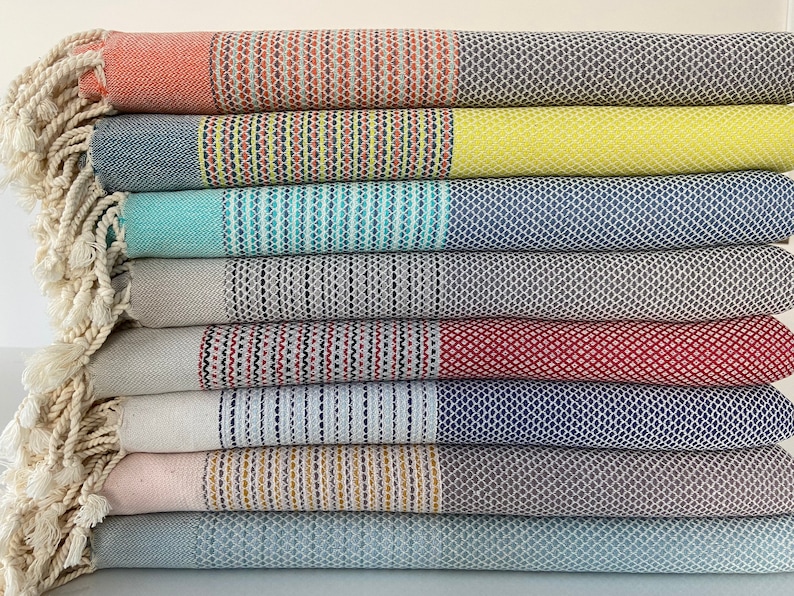 Pu&ograve; includere: Una pila di asciugamani a righe colorati con frange sui bordi. Gli asciugamani sono piegati e impilati in un mucchio ordinato. Gli asciugamani sono realizzati in un materiale morbido e assorbente e sono perfetti per la spiaggia o la piscina.