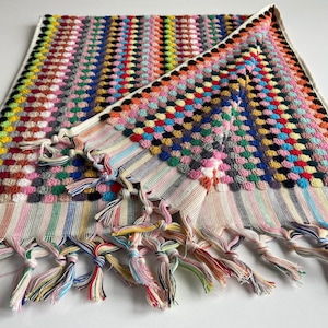 May include: A colorful hand towel with a multi-colored pom-pom design and fringe trim. The towel is folded in half and has a white background.