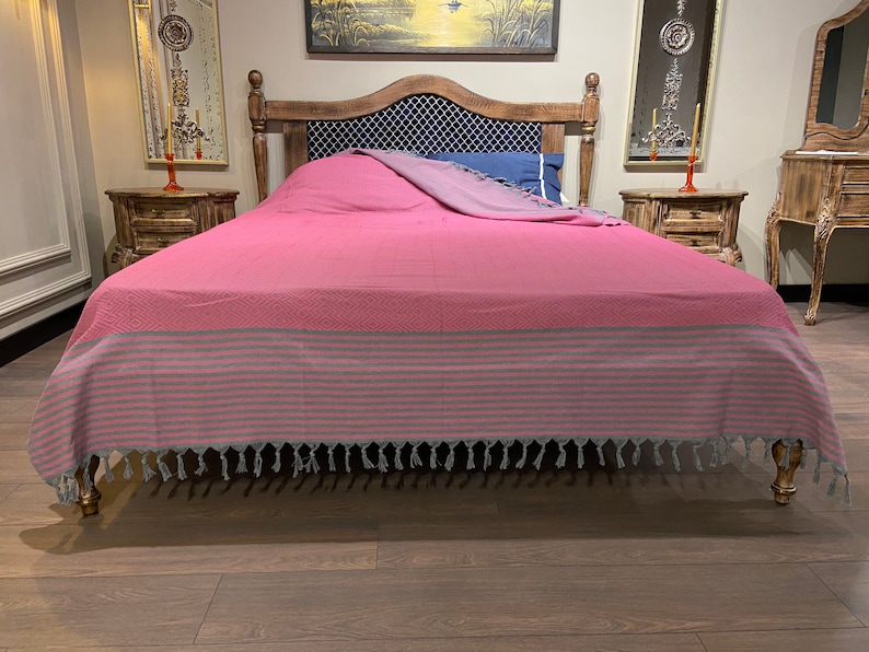 Puede incluir: Un cubrecama a rayas rosa y gris con borlas en un marco de cama de madera. El cubrecama tiene un patr&oacute;n de diamante y est&aacute; hecho de una tela suave y c&oacute;moda.