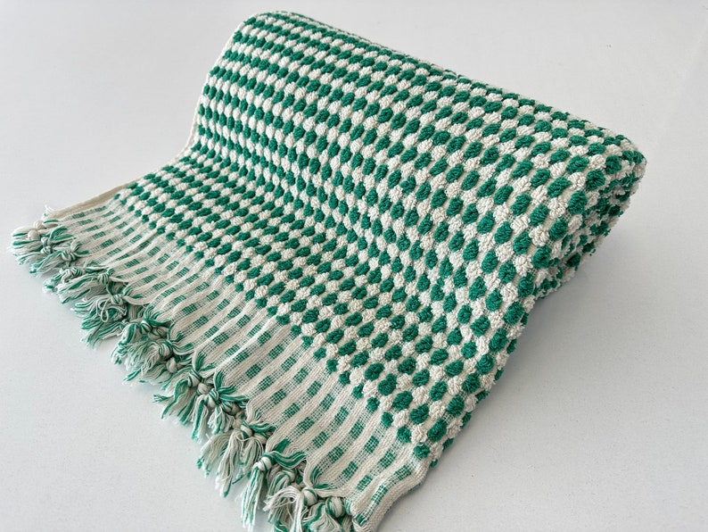 May include: A green and white checkered bath towel with a fringe border. The towel is made of a soft, absorbent material and is perfect for drying off after a shower or bath.