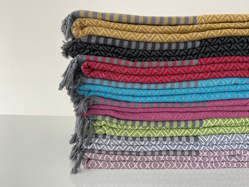 Puede incluir: Una pila de diez toallas turcas coloridas con bordes de flecos. Las toallas est&aacute;n dobladas y apiladas en una variedad de colores, incluyendo amarillo, negro, rojo, azul, rosa, verde, blanco y rosa. Las toallas tienen un patr&oacute;n geom&eacute;trico.