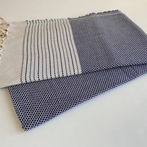 Pu&ograve; includere: Un asciugamano turco bianco e blu navy con frange. L'asciugamano ha un motivo geometrico.