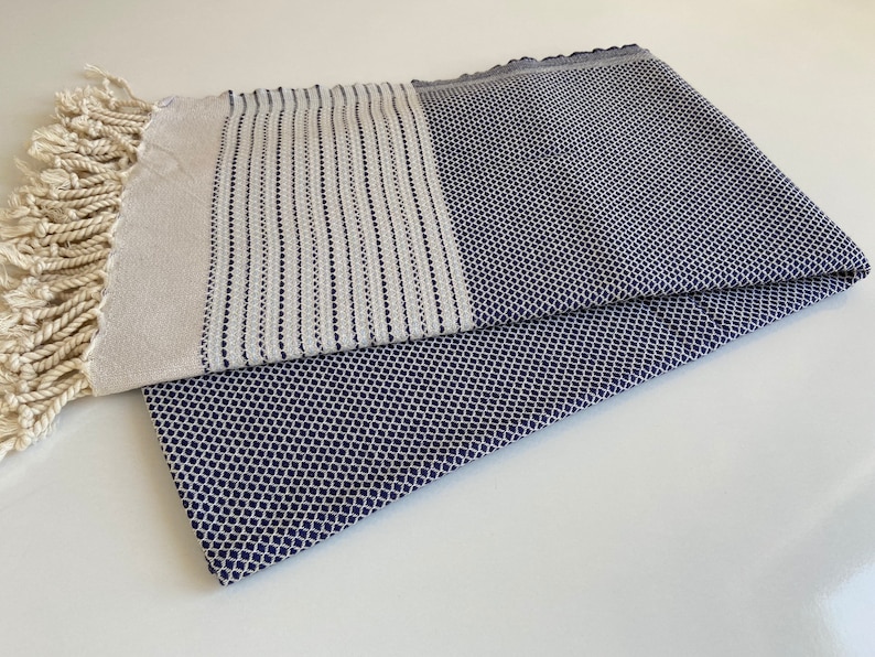 Pu&ograve; includere: Un asciugamano turco bianco e blu navy con frange. L'asciugamano ha un motivo geometrico.