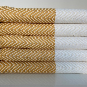 May include: A stack of five yellow and white striped towels with fringe. The towels are folded and stacked on a white surface.