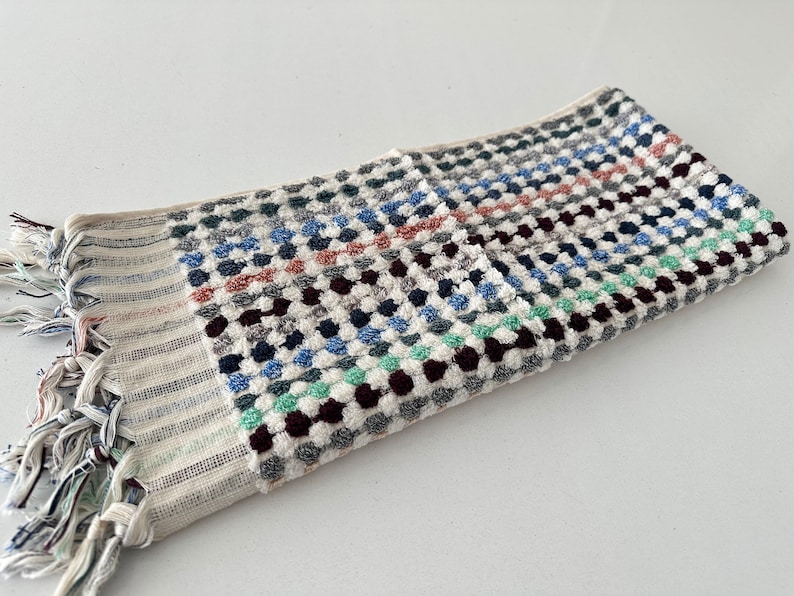 K&ouml;nnte beinhalten: Ein wei&szlig;es Handtuch mit einem geometrischen Muster aus blauen, gr&uuml;nen, braunen und roten Kreisen. Das Handtuch hat einen Fransenrand.