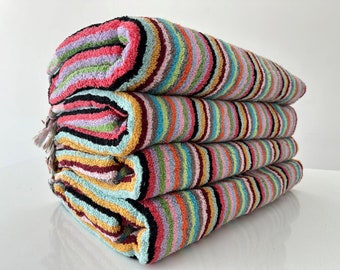 May include: A stack of four striped towels in various colors, including pink, green, blue, yellow, and black. The towels are folded and stacked on top of each other.