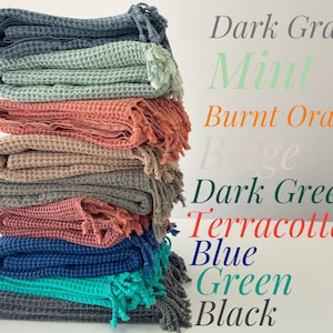 May include: A stack of ten waffle weave throw blankets in various colors, including dark gray, mint, burnt orange, beige, dark green, terracotta, blue, green, and black.