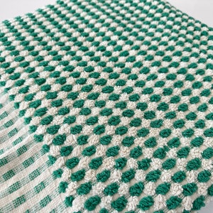 May include: A green and white checkered kitchen towel with a textured surface. The towel has a fringe border.