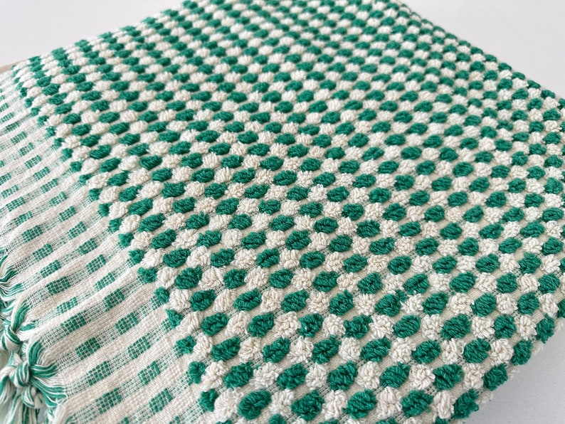 May include: A green and white checkered kitchen towel with a textured surface. The towel has a fringe border.
