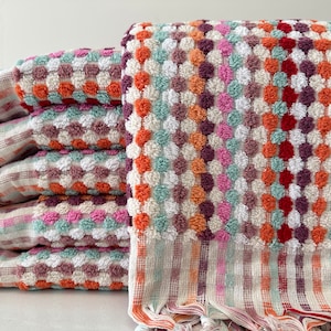 May include: A stack of colorful towels with a textured, patterned design. The towels are made of a soft, absorbent material and feature a fringe trim.