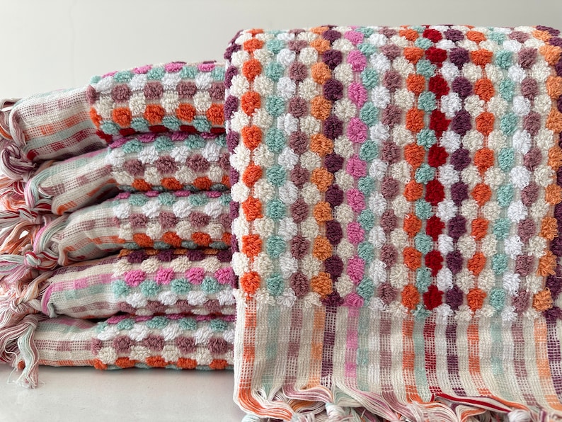May include: A stack of colorful towels with a textured, patterned design. The towels are made of a soft, absorbent material and feature a fringe trim.