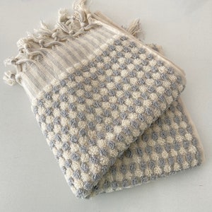 May include: A gray and white waffle weave bath towel with a fringe border. The towel is folded in half and has a checkered pattern.