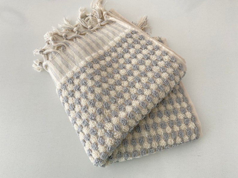 May include: A gray and white waffle weave bath towel with a fringe border. The towel is folded in half and has a checkered pattern.