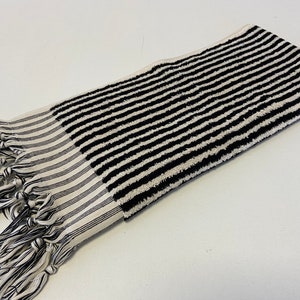 May include: Black and white striped towel with fringe tassels. The towel is made of a soft, absorbent material.