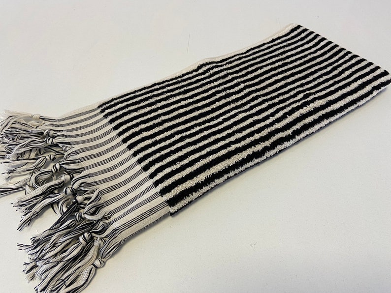 May include: Black and white striped towel with fringe tassels. The towel is made of a soft, absorbent material.
