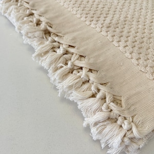 Pode incluir: Uma toalha de banho de cor creme com textura de waffle e borda de franja. A toalha &eacute; feita de algod&atilde;o e tem uma textura macia e absorvente.