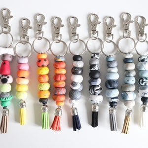 May include: A selection of keyrings with decorative beads and tassels. Each keyring has a silver-tone clasp and ring, with colourful polymer clay beads in various patterns and colours. Tassels are in coordinating colours.