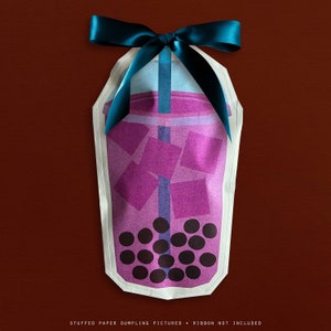 May include: A paper dumpling shaped like a bubble tea drink, with purple liquid, ice cubes, and boba pearls. It's decorated with a teal ribbon bow. The text at the bottom reads: STUFFED PAPER DUMPLING PICTURED • RIBBON NOT INCLUDED.