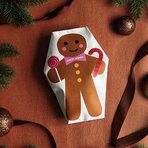 May include: A gift wrapped in white paper featuring a gingerbread man illustration. The gingerbread man has a pink bow tie with the words "Sweet Wishes", a lollipop, and a candy cane. The background is brown with Christmas decorations.