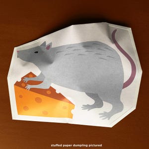 Puede incluir: Una rata de papel gris con cola y orejas rosas, junto a una cuña de queso naranja con agujeros. La imagen está sobre un fondo blanco con el texto "stuffed paper dumpling pictured" en la parte inferior.