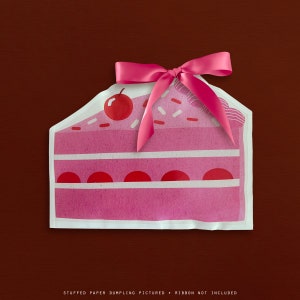 May include: A pink paper cutout of a cake slice with white frosting stripes, red cherries, and sprinkles. A pink ribbon is tied on top. The text at the bottom reads: STUFFED PAPER DUMPLING PICTURED • RIBBON NOT INCLUDED.