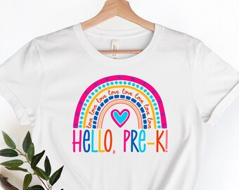 May include: White t-shirt with a rainbow design and the text "HELLO, PRE-K!" in colorful letters. The rainbow is made up of red, orange, yellow, green, blue, and purple stripes with white polka dots. The text "love" is repeated around the rainbow.