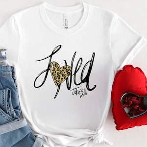 May include: White t-shirt with a black graphic that says "Loved" with a leopard print heart and the text "John 3:16" underneath.