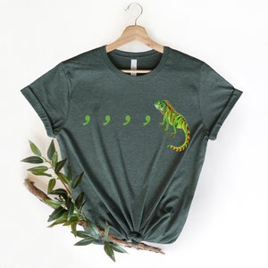 May include: A dark green t-shirt with a green and red iguana and four green commas printed on the front.